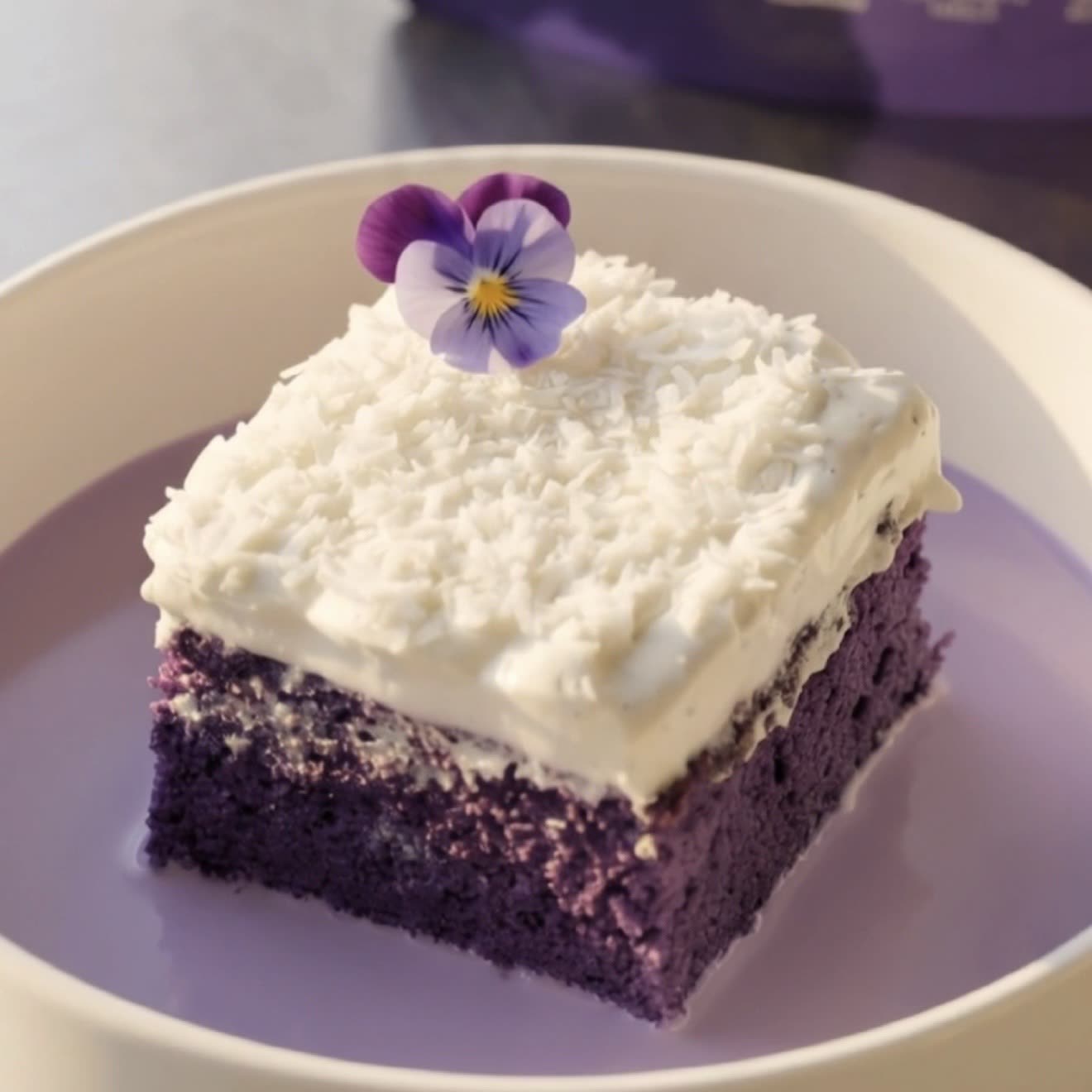 Stück Ube-Kokos-Tres-Leches-Kuchen mit Kokossahne und Kokosraspeln, servierfertig | Ube Nolia