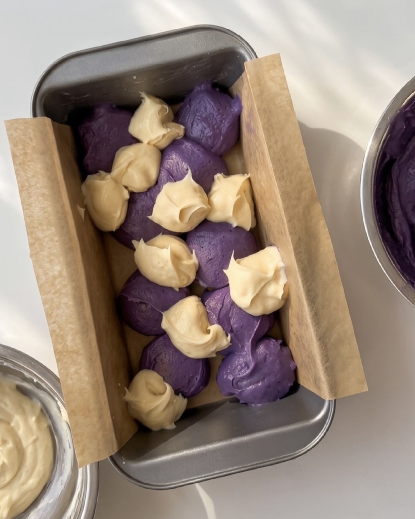 Schöpflöffel lila Ube-Teig und Vanille-Teig abwechselnd in einer ausgelegten Kastenform für UBE NOLIA Ube Marmor-Pfundkuchen