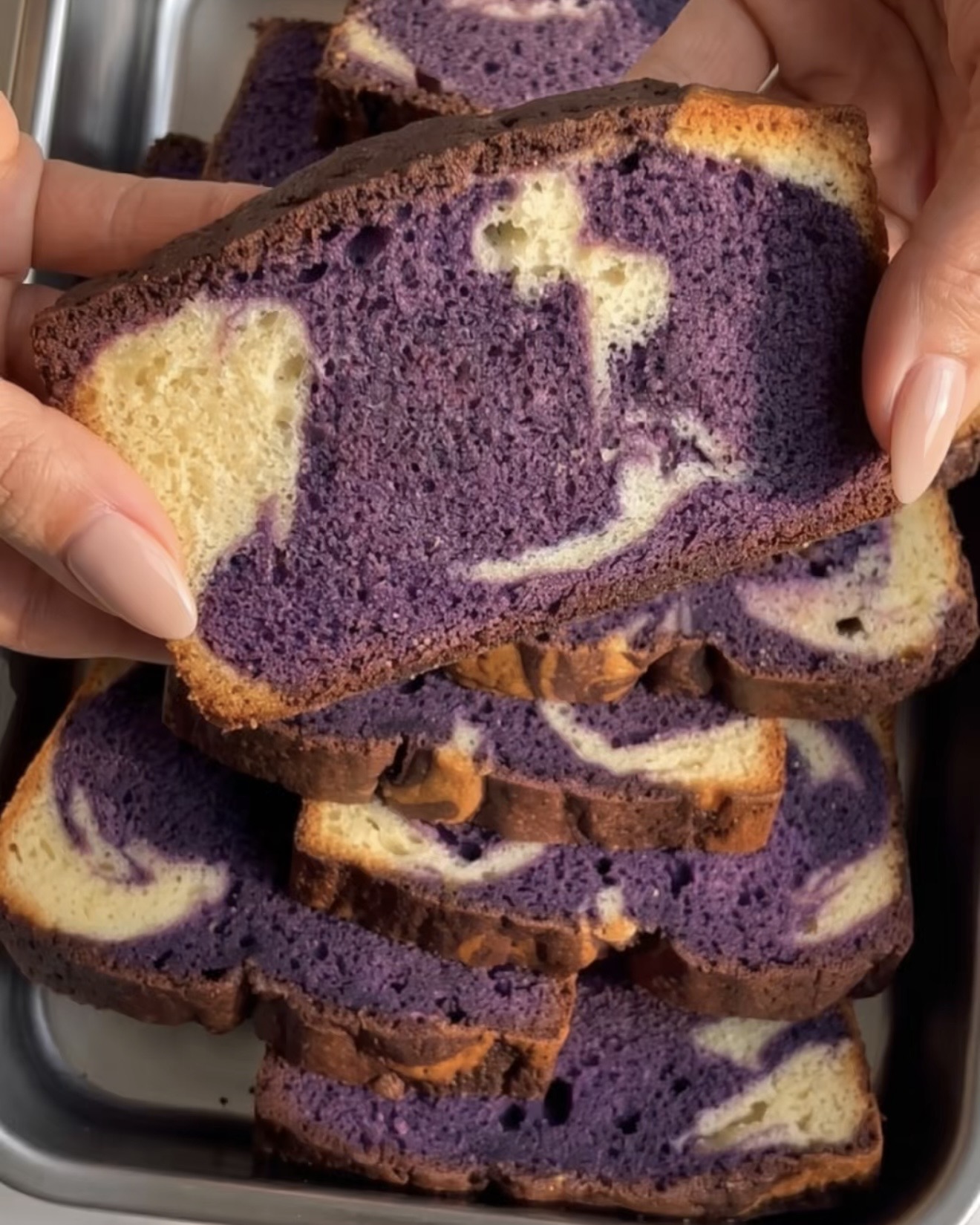 Hand hält ein Stück Ube Marble Pound Cake mit einer lila-vanillefarbenen Wirbelung, gebacken mit Ube Nolia Ube-Pulver