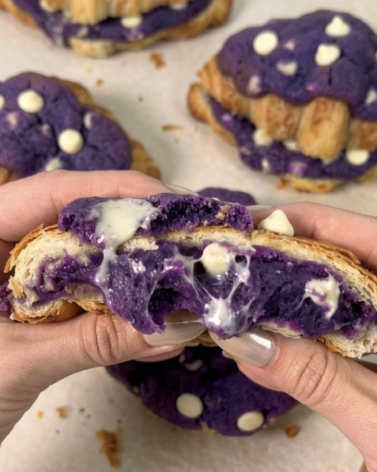 Frisch gebackene UBE NOLIA Ube Crookies auseinandergezogen, um einen geschmolzenen lila Ube (purple yam) Weißschokoladen-Kekskern zu zeigen, der zwischen goldenen Croissant-Schichten hervorquillt