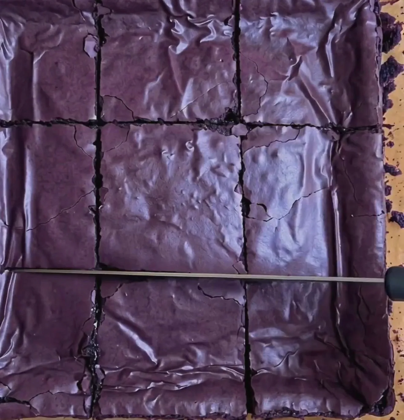 Gebackene klebrige Ube Brownies mit glänzender, tiefvioletter, faltiger Oberfläche, in 9 Quadrate geschnitten mit Ube Nolia powder