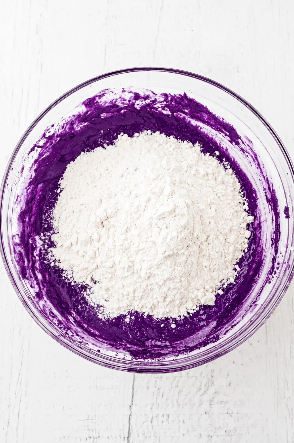 Mehl auf dem tiefvioletten Ube-Weiße-Schokolade-Brownie-Teig in einer Glasschüssel, bereit zum Unterheben mit Ube Nolia powder