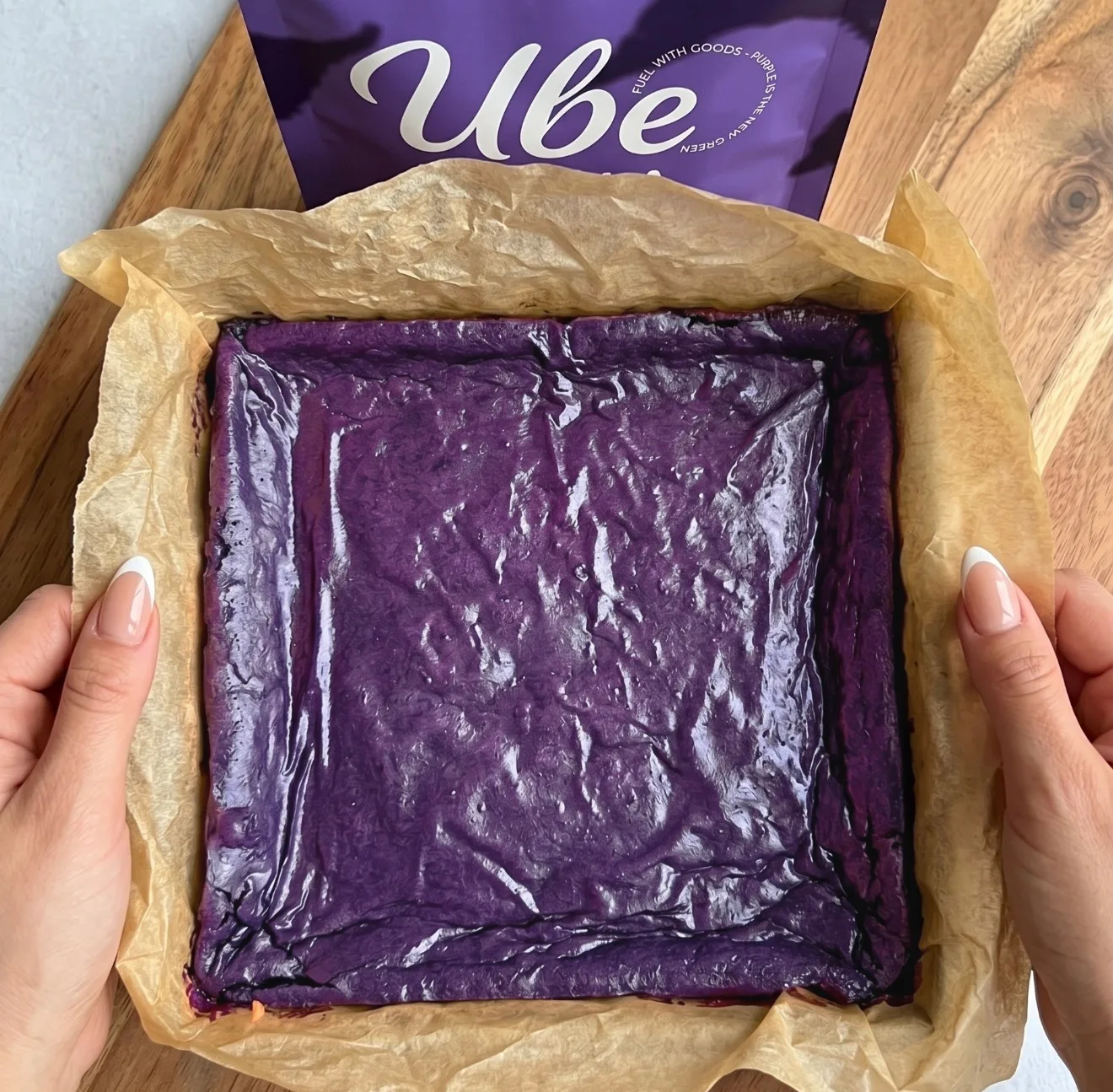 Tiefvioletter Ube-Brownie-Teig in einer mit Backpapier ausgelegten quadratischen Form neben einem Ube Nolia powder Beutel